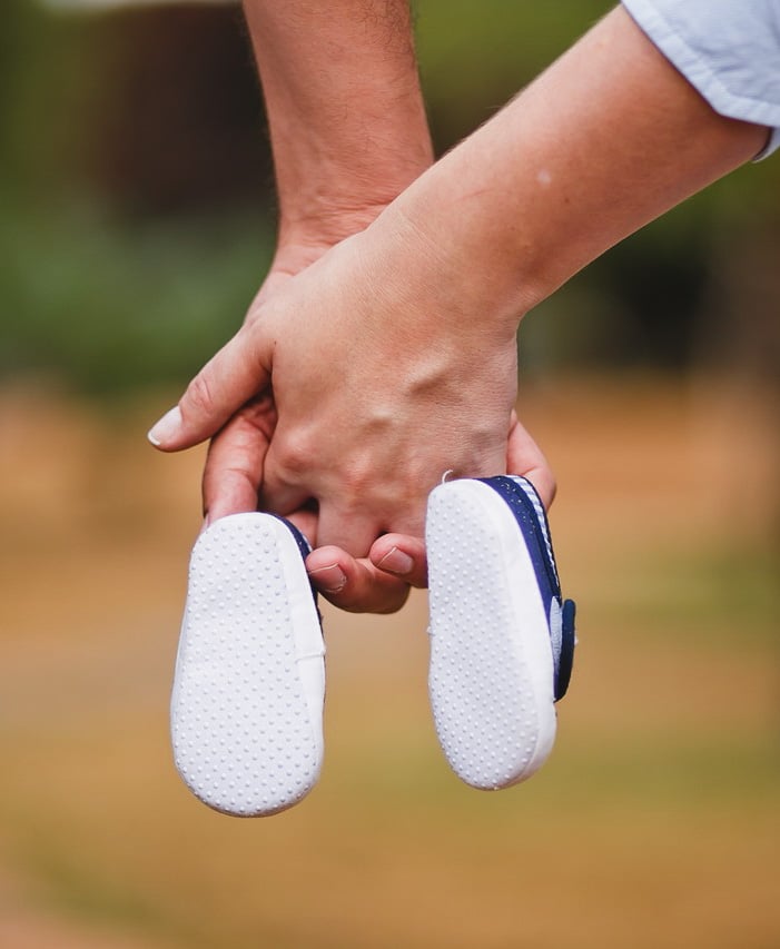 couple se tenant la main avec des chaussures de bébé au bout de leur doigt 