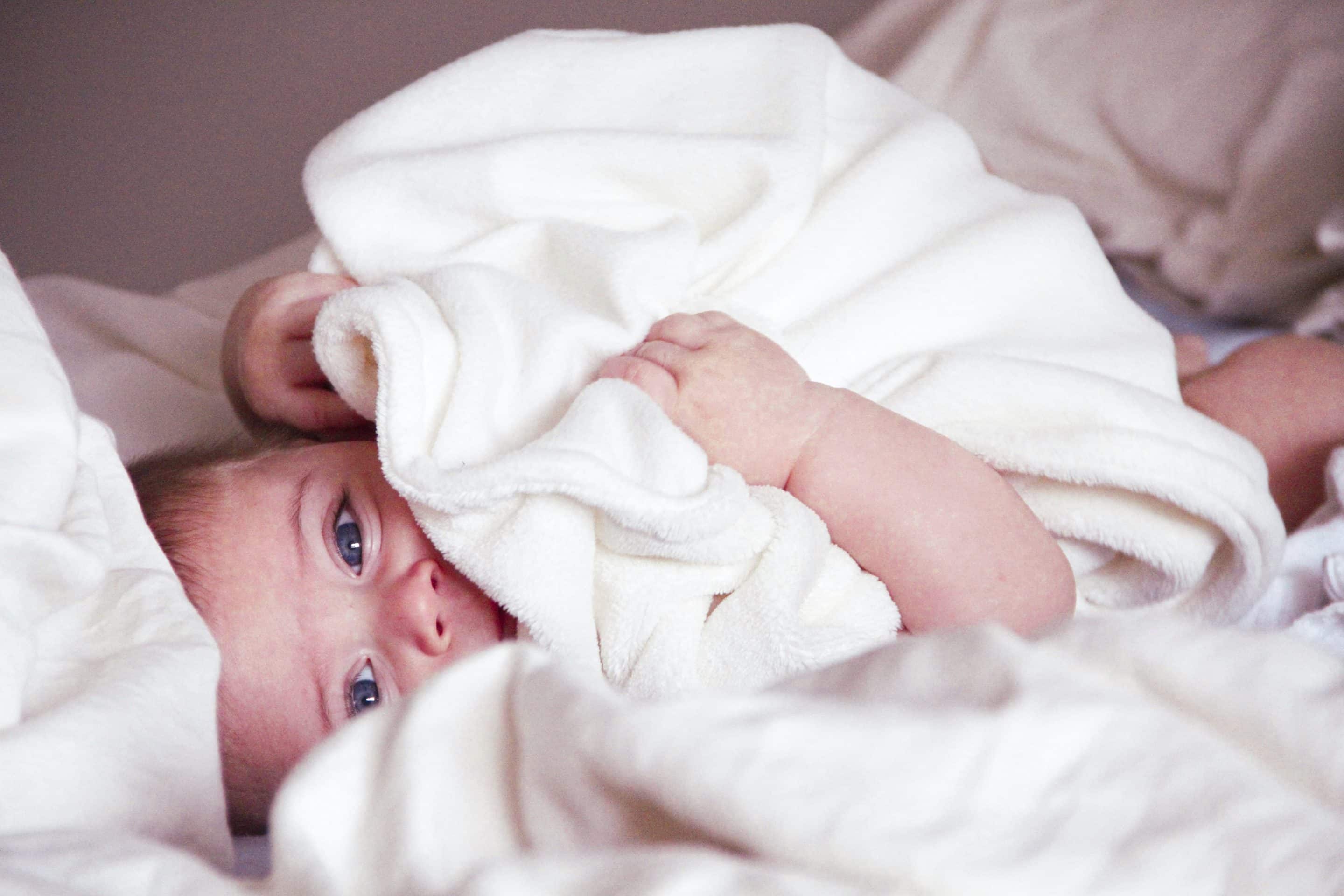 bébé allongé sur le côté caché par une serviette blanche.
